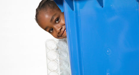 Girl hiding behind blue recycling bin.