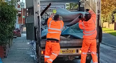 Two people putting large materials into a refuse collection vehicle. 