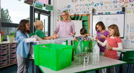 Teacher and children in a classroom sorting through recycling. 