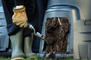 Person in wellies holding a trowel and using a home compost bin
