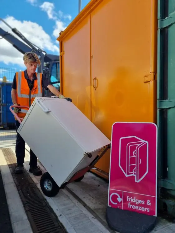 A recycling centre worker moving a white fridge into an orange reuse container